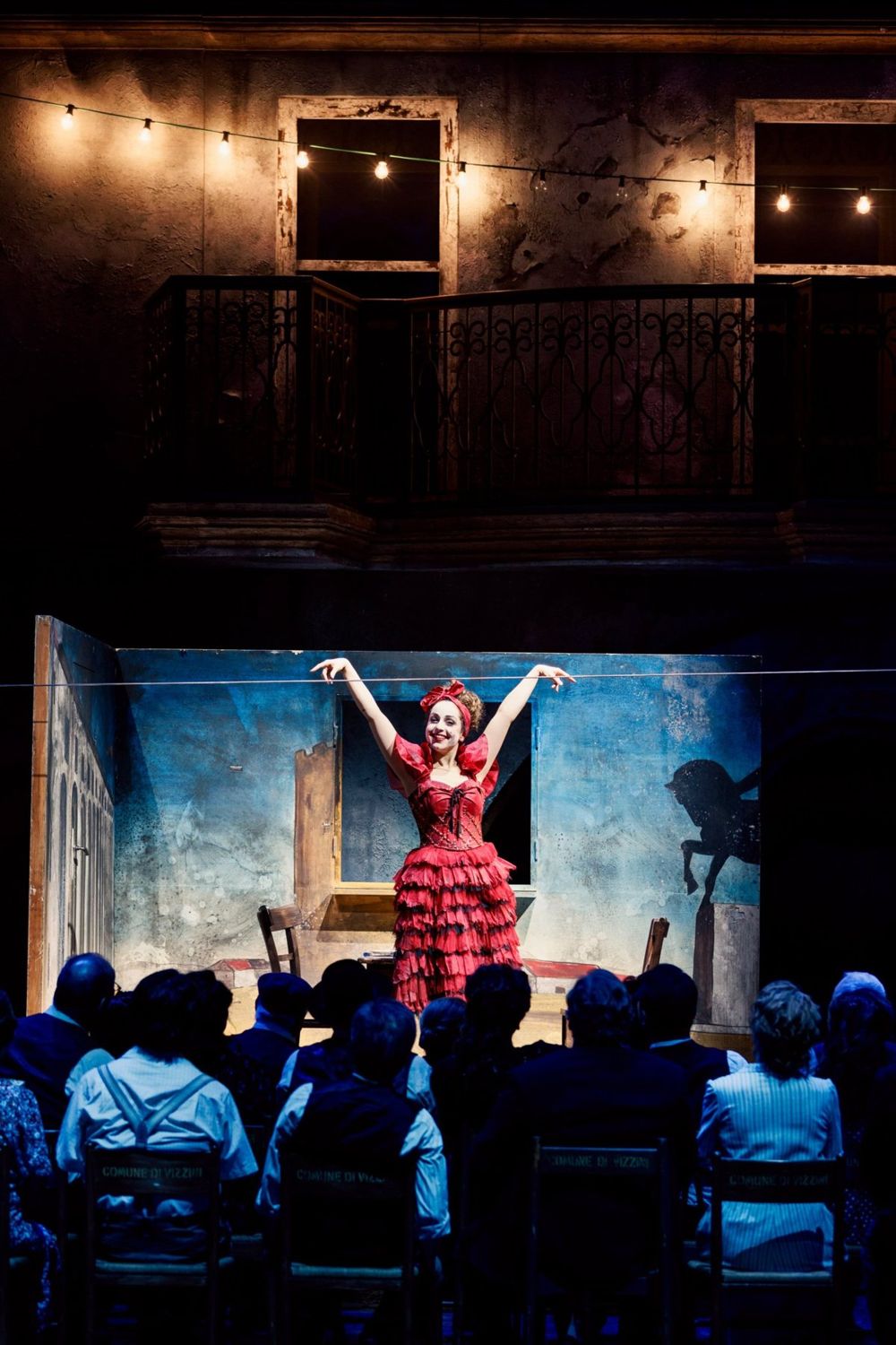 In a red ruffled costume, arms raised on stage